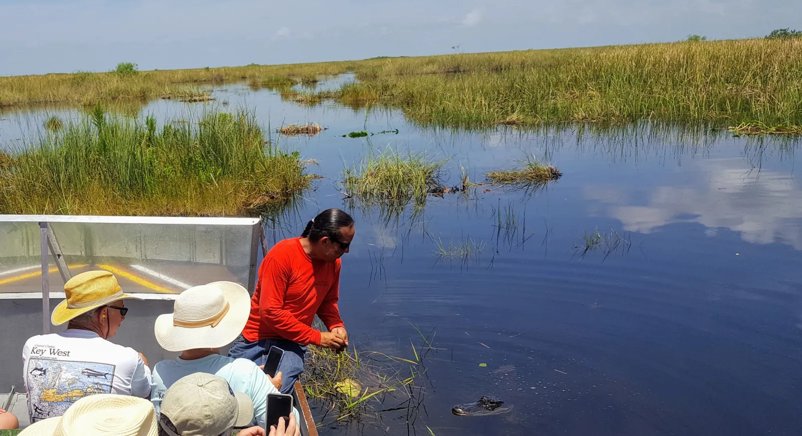 Airboat guide leaning over the side to point out an alligator in open sawgrass water