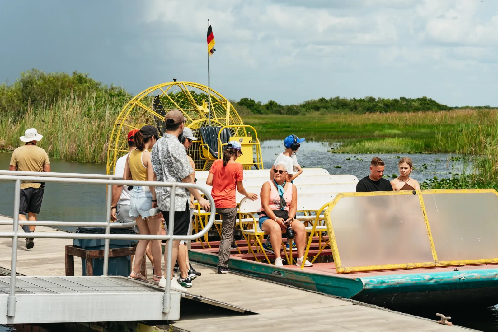 Passengers boarding a yellow airboat from a wooden dock with marsh behind